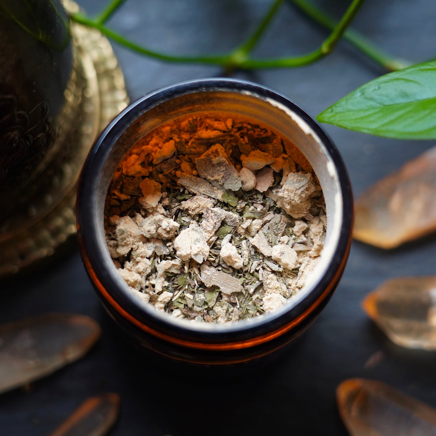 Powder and Herbs stored in amber jar, surrounded by crystals and meditation tools on a black background