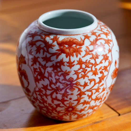 Back side of vintage white and orange handpainted Japanese porcelain vase with flowers, displayed on light wood floor.