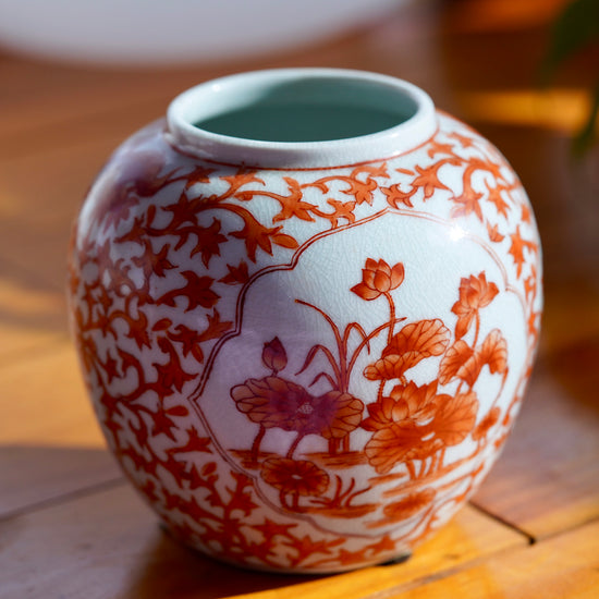 Left side of vintage white and orange handpainted Japanese porcelain vase with flowers, displayed on light wood floor.