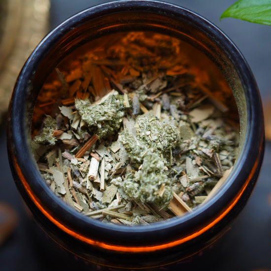 Herbs and tea in an amber jar, photographed in macro with a leaf and meditation bell in the background