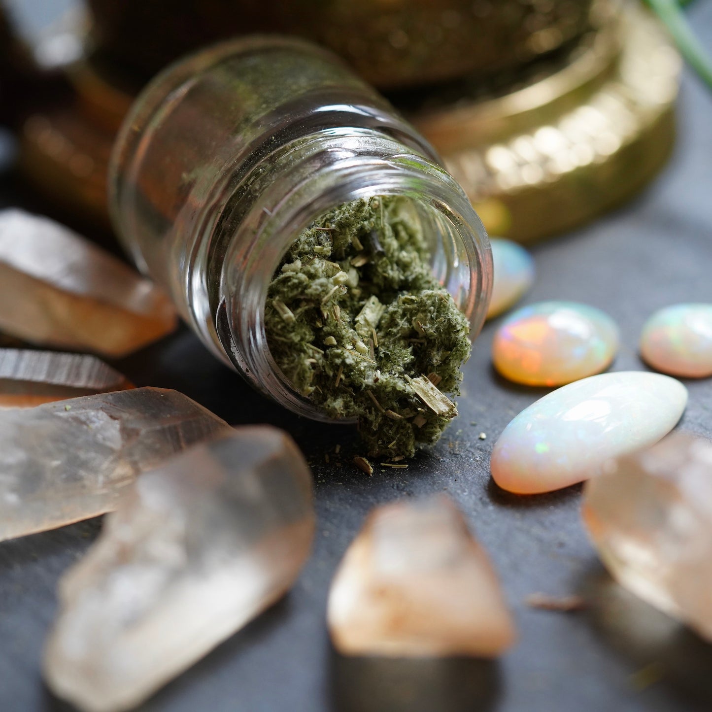 Raw Mugwort Herb spilling out of glass jar surrounded by Ethiopian opals and Hematite Quartz Crystal Points on a black background