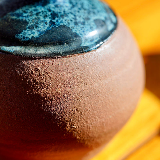 Macro shot of brown clay base on handmade potter bud vase set on light wood floor background